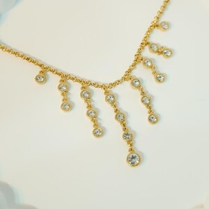 May include: A gold-colored necklace with a delicate chain and dangling, clear crystal accents. The necklace features multiple strands of crystals, creating a cascading effect. The crystals are round and set in gold-colored bezels.