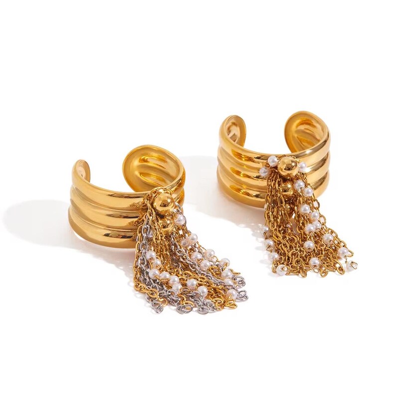 May include: Two gold-colored, open-ended rings with a layered design. Each ring features a cluster of dangling chains and faux pearls. The chains are gold and silver, and the pearls are white. The rings are displayed on a white background.