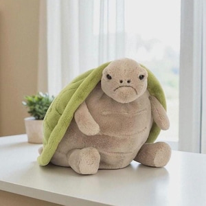May include: A soft toy turtle with a downcast expression. The turtle features a light brown body, a green shell, and small limbs. The toy is positioned on a white surface.
