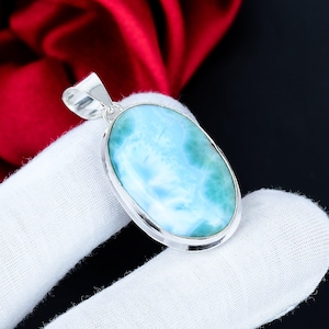 May include: A silver pendant with an oval-shaped, light blue gemstone. The gemstone has a marbled appearance with shades of turquoise and white. The pendant is set in a silver bezel and has a silver loop for a chain.