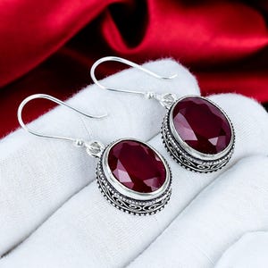 Pode incluir: Um par de brincos de prata com grandes pedras preciosas ovais vermelho escuro. As pedras são engastadas em engastes de prata ornamentados e detalhados. Fecho de gancho.