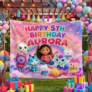 May include: A birthday party backdrop featuring a rainbow, clouds, and cartoon cat characters with a girl playing a guitar. The text reads Happy 5th Birthday Aurora. The scene is decorated with a balloon arch, string lights, and wrapped gift boxes.