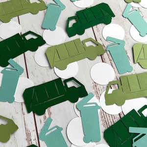 May include: Green and light green paper cutouts of garbage trucks and trash cans. The cutouts are scattered on a white wooden surface.