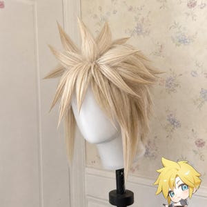 May include: A blonde synthetic wig styled with sharp, spiky layers radiating from the crown, featuring long face-framing strands and a textured, voluminous appearance. The wig is displayed on a plain white mannequin head stand.