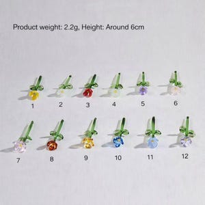 May include: A collection of twelve miniature glass flower sculptures with green stems and leaves. The flowers come in various colors, including yellow, white, red, purple, and blue. Each flower is approximately 2.4 inches tall.