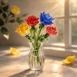 May include: A clear glass vase holds a bouquet of colorful glass roses. The roses are red, blue, yellow, and pink, with green stems and leaves. The vase is on a light-colored surface, with a window in the background.