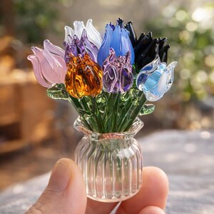 May include: A miniature glass bouquet of tulips in a small, clear vase. The tulips are various colors, including pink, orange, purple, blue, and black. The vase has a ribbed design. The stems and leaves are green.