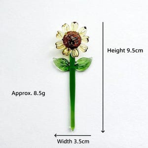 Puede incluir: Un girasol de cristal con centro marr&oacute;n, p&eacute;talos amarillos y tallo y hojas verdes. La altura es de 9,5 cm y el ancho de 3,5 cm. El peso es de aproximadamente 8,5 g. Un acento floral &uacute;nico.