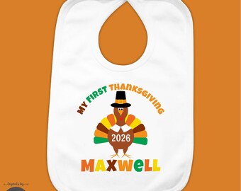May include: A white baby bib featuring a graphic of a brown turkey wearing a black pilgrim hat. The text reads My First Thanksgiving, 2026, and the name Maxwell in orange, green, and yellow letters. The design is centered on the fabric.