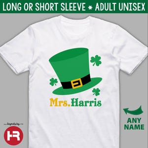 Puede incluir: Camiseta unisex blanca para adultos con un sombrero de duende verde, cintur&oacute;n negro y hebilla dorada, y tr&eacute;boles verdes. El texto "Mrs. Harris" est&aacute; en amarillo y verde. La camiseta tambi&eacute;n tiene el texto "ANY NAME".