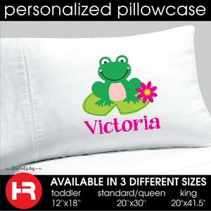 May include: A white personalized pillowcase featuring a green frog sitting on a lily pad next to a pink flower. The name Victoria is printed in pink below the graphic. Available in toddler 12x18 inches, standard/queen 20x30 inches, and king 20x41.5 inches.