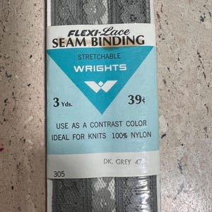 Könnte beinhalten: Eine Packung dunkelgrauer Flexi-Lace-Nahtband. Das Etikett lautet "Stretchable Wrights" und enthält den Text "Als Kontrastfarbe für Strickwaren 100% Nylon verwenden". Die Packung enthält 2,74 Meter Band.