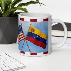 Puede incluir: Taza de cerámica blanca con las banderas cruzadas de Estados Unidos y Venezuela sobre un fondo de cielo azul. La bandera estadounidense está a la izquierda y la bandera venezolana a la derecha. La taza tiene un borde rojo y blanco.