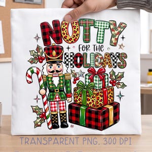 Può includere: Una superficie in tessuto bianco con una grafica colorata di uno schiaccianoci che tiene un bastoncino di zucchero accanto a una pila di tre regali incartati. Il testo recita NUTTY FOR THE HOLIDAYS. Il design include motivi rossi, verdi e leopardati.