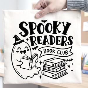 May include: A white canvas tote bag featuring a black graphic print of a smiling ghost wearing a witch hat and reading a book. The text reads "SPOOKY READERS BOOK CLUB" above a stack of three books, accented with small bats and stars.