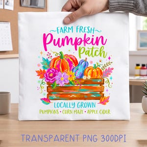 May include: A white tote bag featuring a colorful graphic of pumpkins and flowers in a wooden crate. The text reads Farm Fresh Pumpkin Patch, Locally Grown, Pumpkins, Corn Maze, and Apple Cider in bright pink, blue, green, and orange colors.