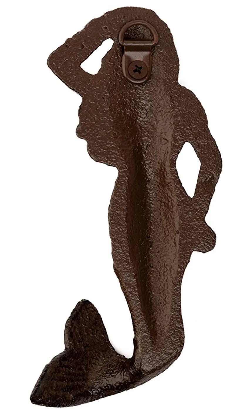 May include: A brown cast iron mermaid wall hook with a hanging loop on the back. The mermaid is in a standing pose with her arm raised in a salute.