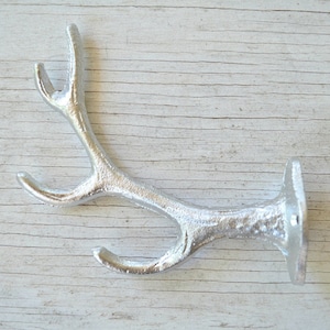 May include: Silver metal antler hook with a textured finish. The hook has two prongs and a flat base.