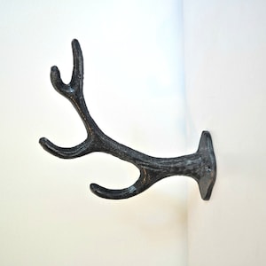May include: A black metal antler hook for hanging items on a wall. The hook is shaped like a deer antler and has a rustic finish.