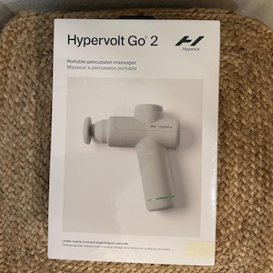May include: A white Hypervolt Go 2 portable percussion massager, with the Hyperice logo, is displayed on its packaging. The box also includes the text "Portable percussion massager" and "Loosen muscle knots and target fatigue in seconds."