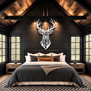 A white metal wall art piece shaped like a deer head with an intricate cutout design featuring a forest scene with trees and branches within the silhouette of the animal, mounted on a dark horizontal wood paneled wall.