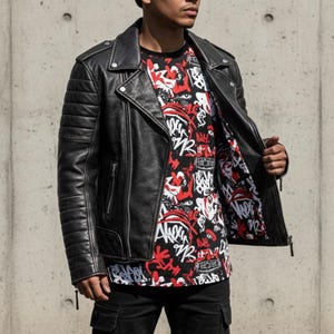 May include: Black leather motorcycle jacket with quilted shoulder and sleeve details. The jacket is open, revealing a black t-shirt with a red and white graphic design. The model is wearing black cargo pants.