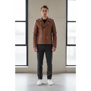May include: A brown leather jacket with a classic asymmetrical zipper design. The jacket features quilted detailing on the shoulders and sleeves. The person is wearing a black shirt, gray pants, and white sneakers.