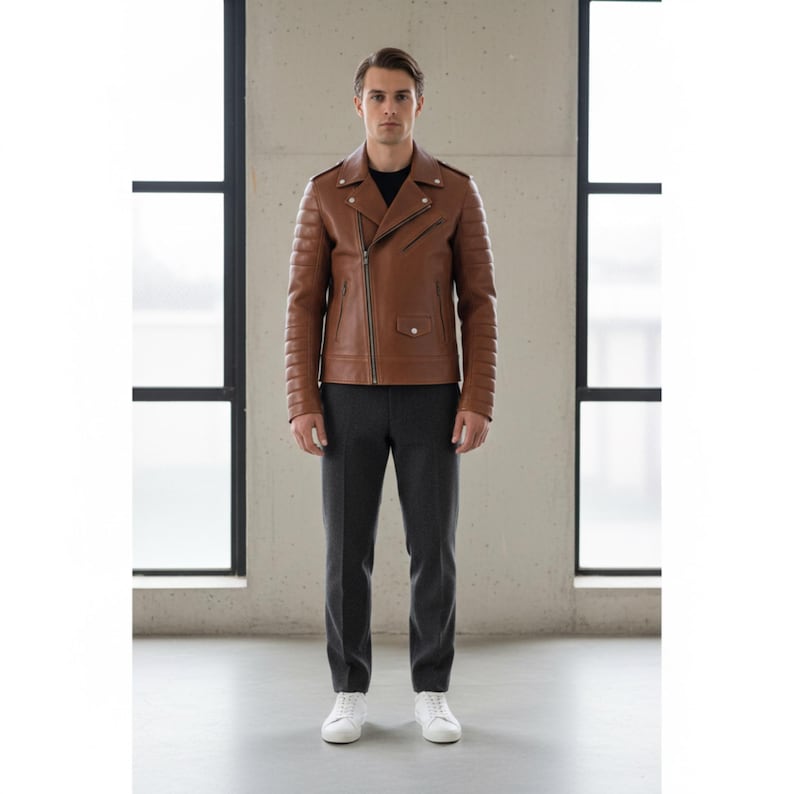 May include: A brown leather jacket with a classic asymmetrical zipper design. The jacket features quilted detailing on the shoulders and sleeves. The person is wearing a black shirt, gray pants, and white sneakers.