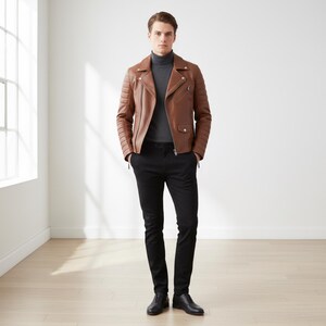 May include: A brown leather jacket with quilted shoulder and arm details. The jacket has a zipper closure and a small pocket on the chest. The person is wearing a gray turtleneck, black pants, and black shoes. The outfit is a modern, stylish look.