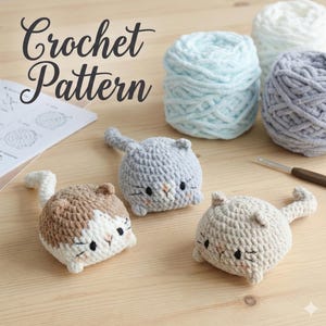 Peut inclure: Image d'un patron de crochet avec trois petits chats crochetés en gris, beige et marron, avec des détails brodés en noir. Des pelotes de laine bleu clair, blanche et grise sont également visibles, ainsi qu'un crochet et des instructions.