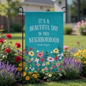 May include: A teal garden flag with the text "IT'S A BEAUTIFUL DAY IN THIS NEIGHBORHOOD" and "Mister Rogers" in white. The flag features a floral design with colourful flowers. The flag is displayed in a garden.