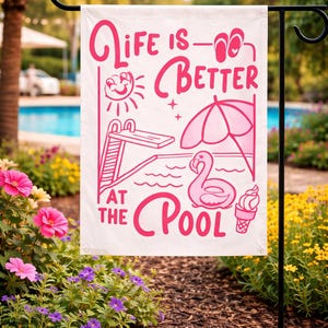 Könnte beinhalten: Eine weiße Gartenflagge mit rosa Text und Illustrationen. Die Flagge lautet "Life is Better at the Pool" mit Bildern von Sonne, Pool, Sprungbrett, Sonnenschirm, Flamingo-Schwimmer und Eiswaffel. Die Flagge wird in einem Garten ausgestellt.