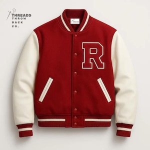 Op de afbeelding: Een rood varsity-jack met crèmekleurige mouwen, voorzien van een grote witte letter R op de borst, een drukknoopsluiting en gestreepte ribboorden bij de kraag, mouwen en zoom. De tekst Threads Throwback Co. staat linksboven afgedrukt.