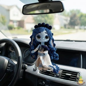 Puede incluir: Muñeca de ganchillo colgando del espejo retrovisor de un coche. La muñeca presenta un vestido azul y blanco, pelo azul y un tocado a juego. Un artículo caprichoso y hecho a mano.