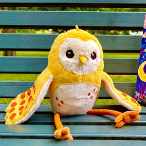 May include: A plush yellow owl with white accents and orange feet and wing details sits next to a book. The book cover is blue with the words "Owl the Owl" and a colorful illustration of an owl on a mushroom.