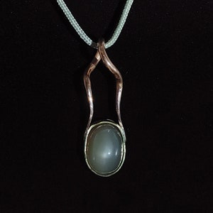 May include: A silver chain necklace with a pendant featuring a gray oval stone set in a silver and copper frame.