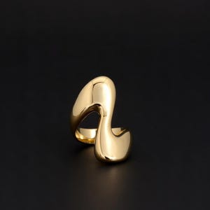 May include: A gold ring with an abstract design. The ring has a flowing, organic shape with smooth, polished surfaces. The design is modern and sculptural, with a bold presence. The ring is a statement piece of jewellery, suitable for everyday wear or special occasions.