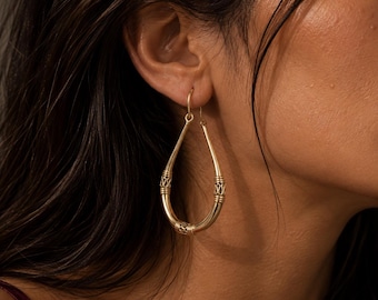 May include: A gold-toned teardrop-shaped hoop earring featuring a smooth metal finish with three distinct decorative bands of intricate wire-wrapped detailing positioned along the lower and side sections of the curved hoop structure.
