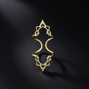 Könnte beinhalten: Ein goldfarbener Ring mit offenem, symmetrischem Design. Der Ring hat blumenförmige Formen oben und unten, die durch gebogene Bänder verbunden sind. Der Ring ist vor einem dunklen Hintergrund platziert.