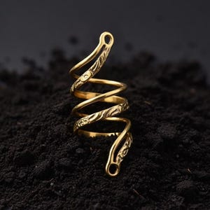 May include: A gold-colored spiral ring with engraved floral patterns. The ring is made of a shiny metal and is set against a dark background. The ring's design features a coiled shape with decorative details.