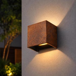 May include: A square wall-mounted light fixture with a textured, rust-colored finish. The fixture emits a warm, glowing light from its top and bottom openings, casting distinct triangular beams of light onto the flat, light-colored wall surface.