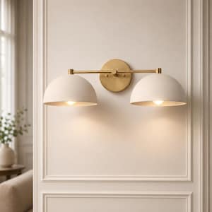 Può includere: Una lampada da parete con una barra orizzontale in ottone fissata a una piastra circolare in ottone. Due paralumi a cupola color bianco sporco opaco sono posizionati alle estremità della barra, ciascuno contenente una lampadina a luce calda.