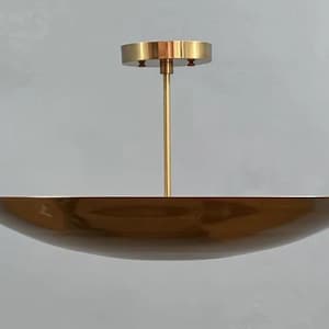 May include: A brass ceiling light fixture featuring a wide, shallow, bowl-shaped shade with a polished metallic finish. The shade is suspended by a thin, vertical rod connected to a circular canopy mount at the top, all in a matching brass tone.