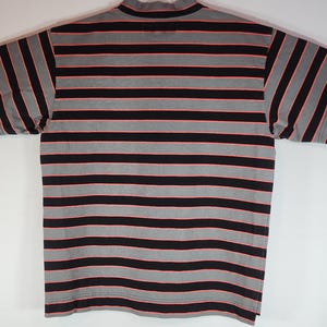 May include: A short-sleeved shirt with a mock turtleneck collar. The shirt features horizontal stripes in black, gray, and red. The shirt is laid flat on a white surface.
