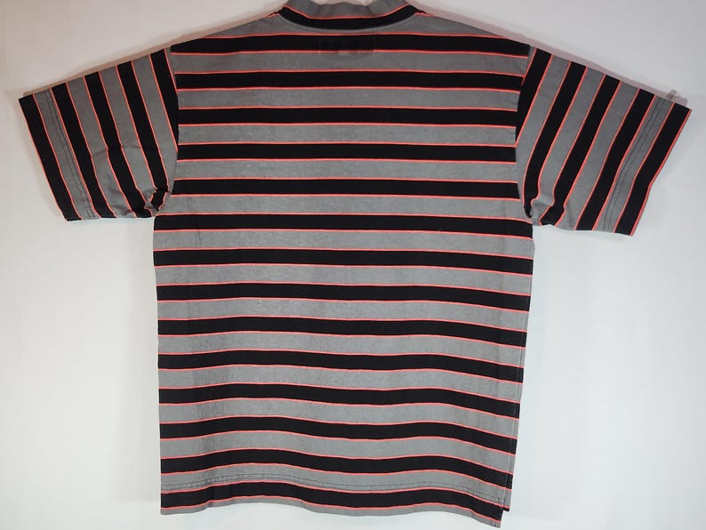 May include: A short-sleeved shirt with a mock turtleneck collar. The shirt features horizontal stripes in black, gray, and red. The shirt is laid flat on a white surface.