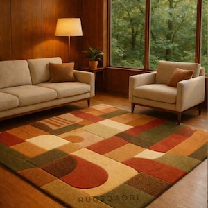 May include: A colorful geometric area rug with a patchwork design in shades of red, orange, green, and beige. The rug is placed in a living room with a sofa, armchair, and large window overlooking a forest.