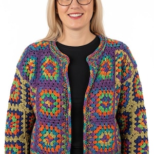 Puede incluir: Un cárdigan de ganchillo abierto y colorido. La chaqueta presenta un diseño de patchwork con cuadrados en tonos morado, naranja, verde y azul. El cuello y los bordes están ribeteados en morado liso. El cárdigan se lleva sobre una camiseta negra.