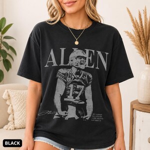 May include: A black short-sleeve t-shirt featuring a graphic of a football player wearing a jersey with the number 17. The text ALLEN is printed in large letters above the player, and the text BE GOOD DO GOOD GOD BLESS GO BILLS is below.