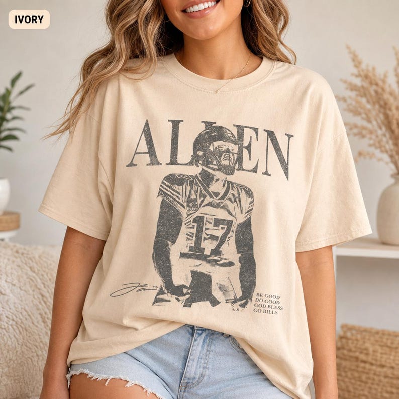 May include: An ivory short-sleeve t-shirt featuring a distressed black graphic of a football player wearing jersey number 17. The text "ALLEN" appears above the player, and the text "BE GOOD DO GOOD GOD BLESS GO BILLS" is printed below.
