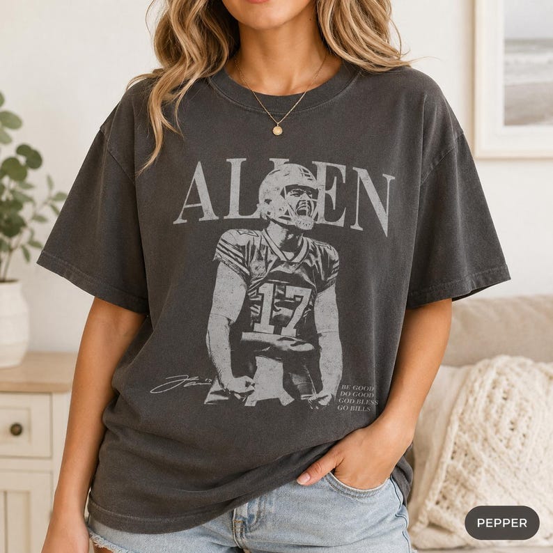 May include: A charcoal gray short-sleeve t-shirt featuring a distressed graphic of a football player wearing jersey number 17. The text "ALLEN" appears in large letters above the player, with "DO GOOD" and "GO BILLS" printed in smaller text.
